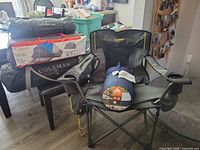 Stacked tents in carry bags and box, Cabela's chair open, sleeping bag on seat