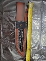 Full view of brown and black leather knife sheath beside tape measure showing approximately 15 in overall length