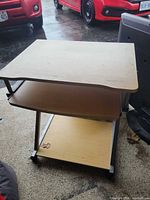 Front view of light wood laminate computer desk showing top, middle shelf, bottom shelf, and black metal frame