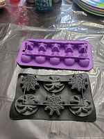 Purple 10-cavity skull mold and black 6-cavity spider web mold on table