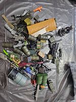 pile of plastic military style action figure accessories showing variety of weapons, ammo belts, barrels, crates and other gear