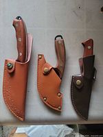 Three knives in sheaths, showing handle shapes and sheath designs