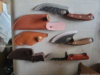 Three curved knives with hammered blades and three leather sheaths laid out
