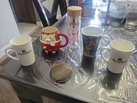 Overview showing two Laura Secord mugs, hedgehog mug, wolf mug, glass tumbler with bamboo lid and metal mesh strainer