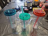 Front view of three clear double-wall tumblers with colored lids and straws on table