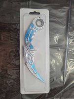 Front view of sealed decorative silver and blue karambit knife in blister package