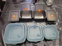 Four stainless containers with gray lids and three teal lids displayed