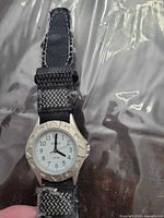 Front view of Timex wristwatch showing silver-tone case, white dial, black numerals, and frayed black/grey nylon strap