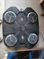 Top view of black plastic punching machine showing four circular light-up strike pads, central controls and attached power cord