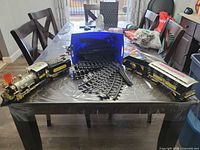 Full view of locomotive, tender, passenger coach, curved track pieces and blue storage bin on table