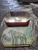 Lid and base of red octagonal tin box showing equestrian print and interior
