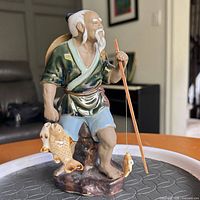 Front view of fisherman figurine displaying fish, rod, and attire