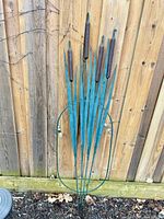 Full view of metal cattail ornament leaning on fence