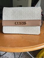 Front of Guess purse showing monogram pattern, tan trim, gold logo plaque