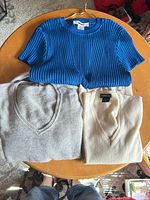 All three garments laid out: blue DKNY top, grey and cream cashmere sweaters