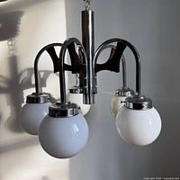 Full view of chandelier showing five white glass globes, chrome column and wood arms