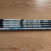 Four black Matrix shafts and one silver Aldila shaft laid side-by-side showing graphics