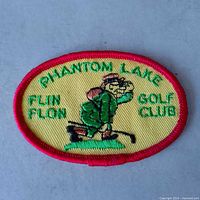 Front view of oval yellow Phantom Lake Golf Club patch with red border and golfer design
