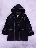 Full view of black hooded suede shearling coat laid flat