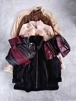 Five stacked jackets in beige, brown, blush and black with folded black and burgundy faux leather pants flanking