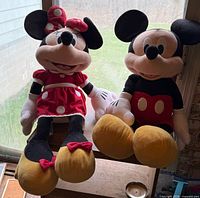Mickey and Minnie Mouse plush toys sitting side by side on table, window background