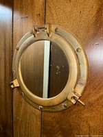 Front view of brass porthole mirror mounted on wood paneling