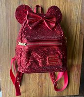 Front of red sequin Loungefly Disney mini backpack showing ears, bow, front pocket and logo plaque