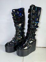 Full view of both knee-high holographic buckle boots