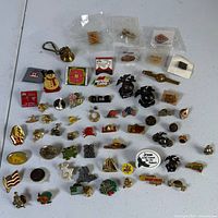 Overall view of roughly 70 assorted pins and two brass charms laid out on table