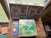 Two Teddy Ruxpin carry cases and one Book ’N’ Tape Along case on table with promo cards