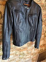 Front view of black leather biker jacket hanging, showing overall design and pockets