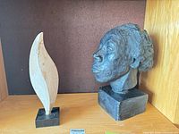 Plaster bust and stone leaf sculpture side by side on shelf