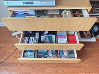 Three open drawers showing CDs, DVDs, VHS, tapes, games