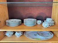 Overall view of stacked plates, cups, creamer, sugar bowl and oval platter in cabinet