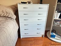 Front view of white five-drawer dresser beside bed