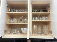 Cabinet view showing multiple shelves of assorted glassware, ceramic bowl and vases