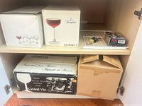 Cabinet showing two Luminarc boxes, Grand Vin box, brown box, wine pump, stoppers and wire shelf