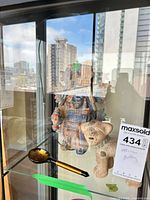 Front view of figural vase, animal figurine and spoon in display cabinet