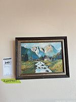 Framed alpine landscape painting on wall with lot tag visible
