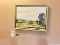 Framed oil landscape painting hanging on wall with lot tag visible