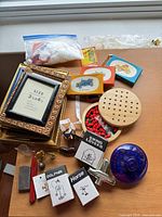 Assorted items laid out on table including frames, peg board, boxed kits, wax, figurines, bells, stapler, glass jar, decor fiber