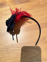 Side view of black headband with red feathers and black felt flower