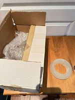 Open cardboard box with bubble wrap and frosted glass diffuser on wooden surface