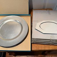 Stack of round plastic chargers and stack of octagonal silver-plated chargers.