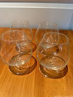 Four clear glass brandy snifters on wooden surface