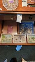 All five framed artworks inside drawer: three small watercolors, one vertical print, one square fabric piece