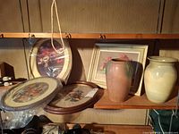 Shelf showing four framed floral artworks and two ceramic vases