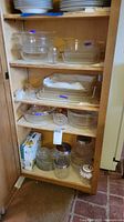 Cabinet showing all four shelves filled with glass bakeware, plates and storage jars
