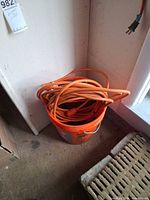 Orange 5-gallon bucket holding three orange grounded extension cords