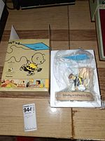 Figurine in plastic within foam tray beside warped Peanuts box